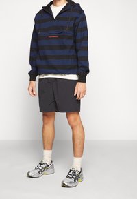 Felpa con cappuccio a righe nere e blu con tasca frontale e coulisse, abbinata a pantaloncini scuri e scarpe da ginnastica argento.