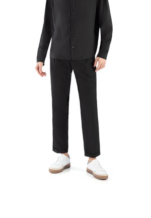 Black button-up shirt and matching black trousers, paired with white sneakers featuring brown soles. Smooth texture, standard fit.