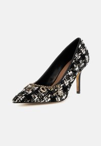 Scarpa con tacco alto bianca e nera a motivo, con punta affilata, tessuto testurizzato, dettaglio in catena dorata e charm decorativi.