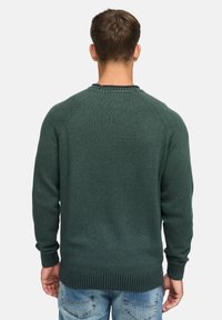 Grøn ribbestrikket sweater med rund halsudskæring, der har raglanærmer og en tekstureret finish, parret med lyseblå jeans.