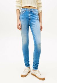 Jeans ajustados de color azul claro en denim, con cintura de altura media, un ligero desgaste y cinco bolsillos, combinados con zapatillas blancas.