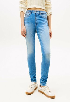 Jean skinny bleu clair en denim, avec une taille moyenne, un léger dégradé et cinq poches, associés à des baskets blanches.