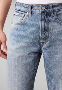 Κοντινή εικόνα σε ανοιχτό μπλε τζιν Calvin Klein με διακριτικό γεωμετρικό μοτίβο και ορατή ετικέτα της μάρκας στην μπροστινή τσέπη.