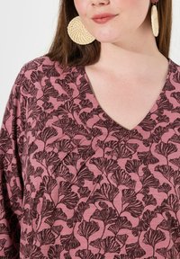 Top a maniche corte e scollo a V in rosa polveroso con un motivo a foglie nere. Un paio di grandi orecchini circolari intrecciati completano il design.