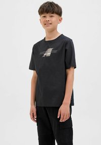 Zwarte t-shirt met korte mouwen van katoen, met een grafische logo in metallic kleuren aan de voorkant. Gecombineerd met zwarte cargobroek.