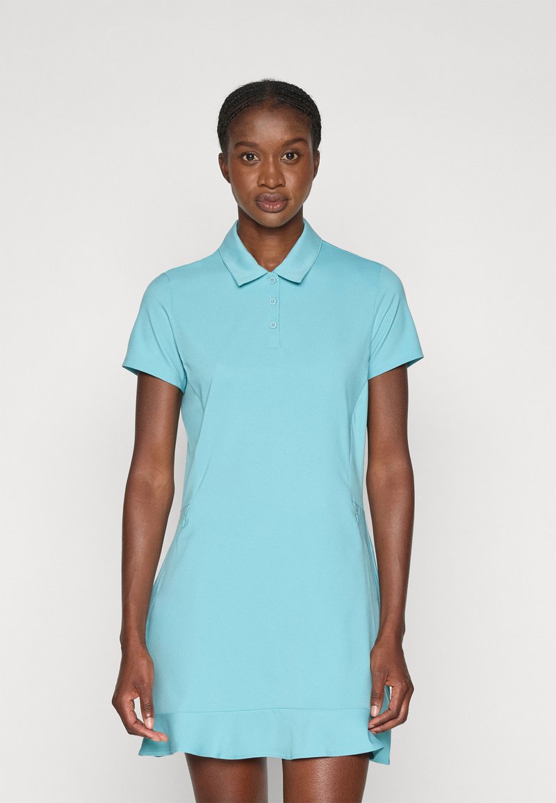 Polo obleka v svetlo modri barvi, izdelana iz gladkega in raztegljivega materiala. Ima ovratnik, kratke rokave in razširjen rob z stranskimi žepi.