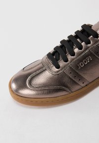 Sneaker in pelle bronzo metallico con lacci neri e suola in gomma, con branding "JOOP!" in rilievo sul lato.