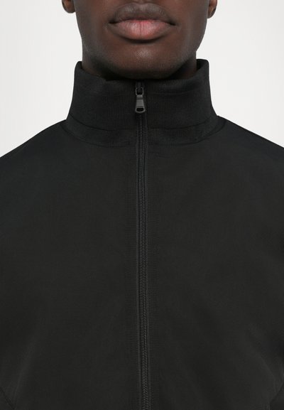 Jachetă neagră cu fermoar, cu guler înalt, realizată dintr-un material texturat, având un fermoar central și un design minimalist.