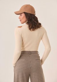 Suéter acanalado de color crema con cortes en los hombros, combinado con pantalones de tiro alto de patrón marrón. Una boina marrón completa el look.