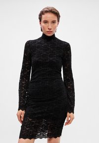 Μαύρο φόρεμα δαντέλας με μακριά μανίκια και ψηλό λαιμό, με λουλουδένια μοτίβα και σφιχτή σιλουέτα. Λεπτομέρεια με περιθώριο που έχει καμπύλες.