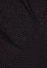 Svart vävt tyg med en texturerad yta, med diagonala sömmar och subtila designinslag, vilket skapar ett strukturerat utseende.