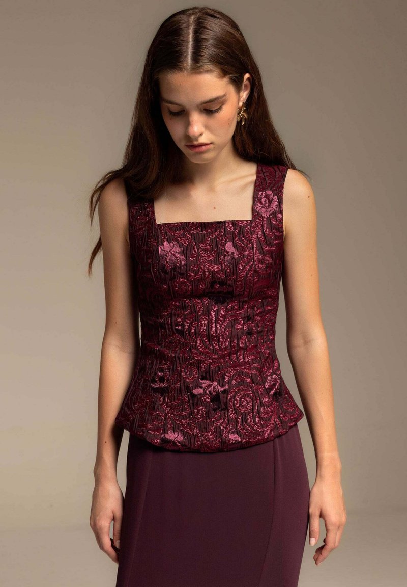 Top peplum burdeos con escote cuadrado, patrón floral texturizado y acentos brillantes. La tela suave se extiende hacia un diseño ajustado por debajo de la cintura.