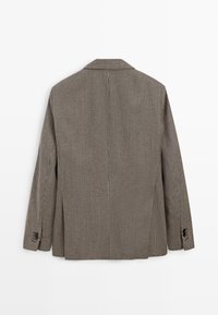 Marynarka w wzór pepitki w odcieniach brązu i beżu, z dwoma rozcięciami z tyłu i smukłymi klapami, wykonana z fakturowanej tkaniny.