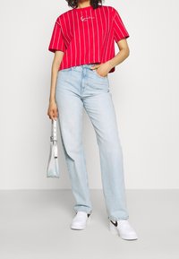 Punainen lyhyt t-paita, jossa valkoiset pystysuorat raidat, yhdistetty vaaleansinisiin korkeavyötäröisiin farkkuihin. Asusteet: pieni kirkas käsilaukku, valkoiset tennarit.