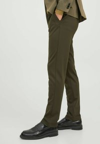 Pantalones de corte ajustado en verde oliva, confeccionados en una tela suave, con bolsillos laterales y combinados con mocasines negros.