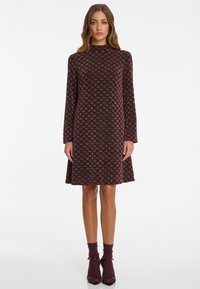 Long-sleeved dress in dark burgundy with a diamond pattern, textured fabric, and flared hem. Paired with burgundy socks and shoes.