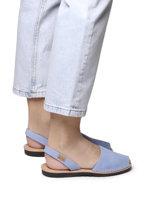 Light blue leather sandals with an open back, rounded toe, and minimalistic design. Brown sole with subtle branding detail.