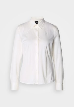 Chemise blanche à manches longues avec col classique en tissu coton doux, présentant une coupe ajustée et un design simple sans motifs.