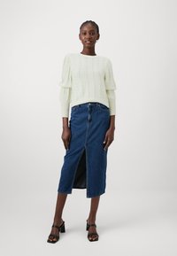 Lys grønne strikkegenser med bølgete tekstur og puffermer, kombinert med et midt lengde denimskjørt med en frontsplit. Sorte blokk-hæl sandaler.