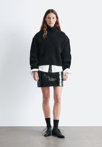 Black ribbed turtleneck sweater paired with a white shirt and a shiny black sequin mini skirt, complemented by black socks and shoes.