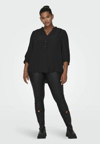Blusa negra de botones con escote en V y mangas de tres cuartos, combinada con leggings negros ajustados y botas de altura de tobillo. Tejido texturizado.