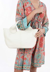 Witte leren tote bag met afgeronde hoeken, gestructureerd oppervlak en dubbele handgrepen. Gecombineerd met een jurk met een multikleurig patroon.