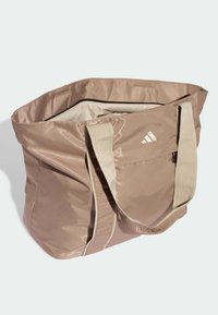 Saco tote de nylon rosa com duas alças de tecido bege, topo com fecho éclair e um logótipo branco na frente. O interior é de cor creme.
