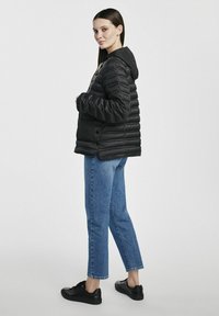 Czarna kurtka puchowa z kapturem, z pikowanym wzorem. Nosi się z niebieskimi dżinsami i czarnymi trampkami. Prosty, funkcjonalny styl.