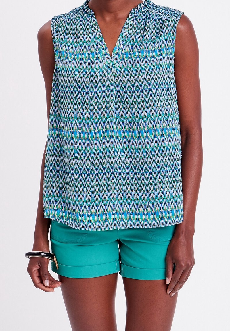 Ærmeløs top med V-hals, der har et geometrisk mønster i blå og grøn på en lys baggrund. Sæt sammen med teal shorts og et armbånd.