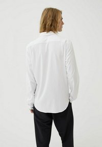 Witte langemouwen overhemd met een standaard kraag, zachte stof, een ronde zoom en een getailleerde fit, gecombineerd met zwarte broek.