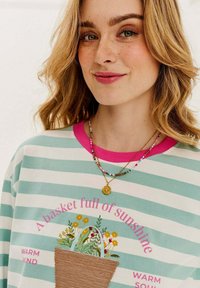 Svetlo modrý a biely pruhovaný mikina s ružovým golierom; obsahuje kvetinovú grafiku a dizajn z tkaného košíka. Viacfarebné náhrdelníky z korálok v skladbe.