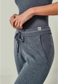 Graue gestrickte Jogginghosen mit ribbeltem Bund und Kordelzug, Seitentaschen und einem strukturierten Paneel-Detail im Hüftbereich.