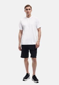 Weißer Kurzarm-Hoodie mit Kordelzug, kombiniert mit schwarzen Shorts und schwarzen Sneakers. Glatter Stoff, lässige Passform und minimales Design.
