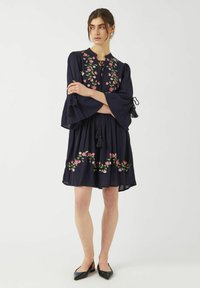 Granatowa sukienka z kwiatowym haftem, dzwonowymi rękawami i frędzlami; lekki materiał, luźny krój i długość do kolan.