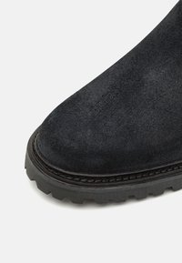 Botte de cheville en suède noir avec un bout rond, semelle en caoutchouc texturé épais et coutures contrastantes le long du bord.