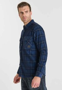 Marineblauw flanellen overhemd met een ruitpatroon, twee borstzakken, knoopsluiting en een klein logo-label op de linker zak.