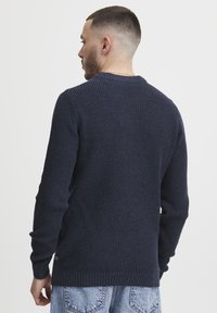 Sötétkék kötött pulóver texturált mintával, kerek nyakkivágással, bordás mandzsettákkal és aljjal. Lazacímke, puha anyag és kényelmes szabás.