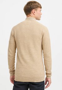 Suéter de punto beige con un cuello alto, mangas largas y un patrón texturizado. Corte estándar, fabricado en tela suave.