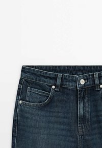 Donkerblauwe denim jeans met een klassiek vijf-pocket ontwerp, zilveren hardware en een rechte snit bij de taille met een lichte textuur.