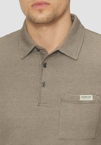 Braunes, strukturiertes Poloshirt mit Kragen, Drei-Knopf-Blende und Brusttasche mit einem Etikett. Glattes Gewebe mit einem Karomuster.