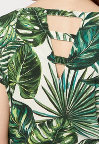 Zelený tropický top s potiskem velkých listů na světlém pozadí, s designem s připnutými zády a těsným střihem.