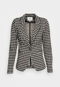 Blazer à carreaux noirs et blancs avec manches longues, col cranté et fermeture à un bouton, présenté sur un fond uni.