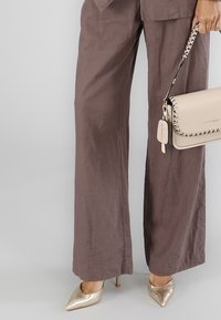 Vida, bruna linbyxor med vida ben, i kombination med gyllene klackskor med spetsig tå och en beige handväska med kedjedetaljer och sydda accenter.