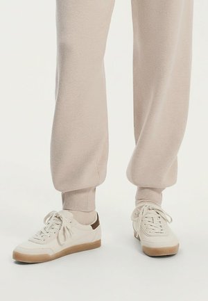 Bílé tenisky s hladkým koženým svrškem, hnědým akcentem na patě, světle béžovými tkaničkami a hnědou gumovou podrážkou. Kombinované s béžovými tepláky.