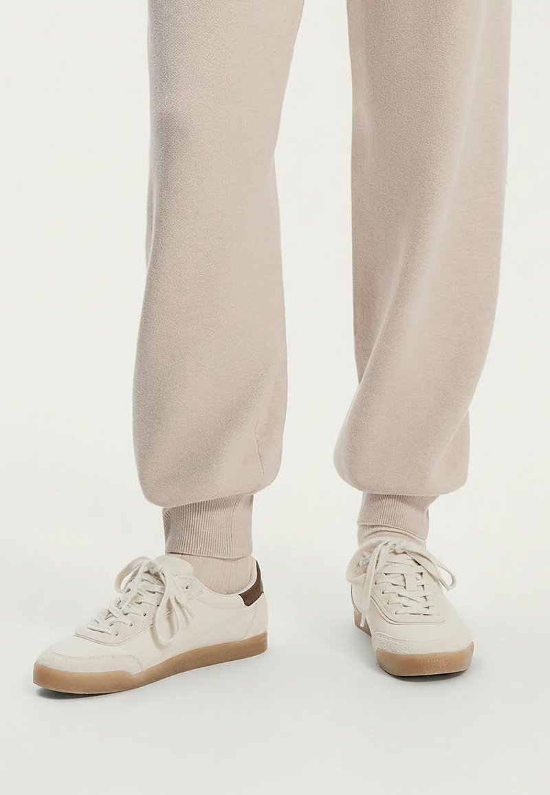 Valkoiset tennarit, joissa sileä nahkapäällinen, ruskea korostus kannassa, vaaleanbeiget nauhat ja ruskea kumipohja. Yhdistetty beigeihin collegehousuihin.