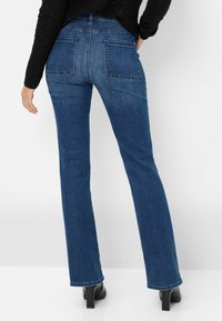 Jeans in denim blu con fondo svasato e vita media, dotati di due tasche posteriori e una leggera texture sbiadita. Rifiniti con dettagli cuciti.