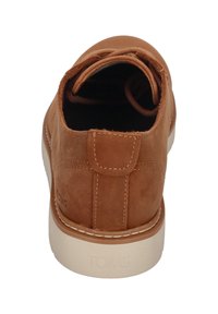 Chaussure en daim marron avec un talon arrondi, des détails cousus et une semelle en caoutchouc beige clair. Dotée d'une boucle à l'arrière pour un enfilage facile.