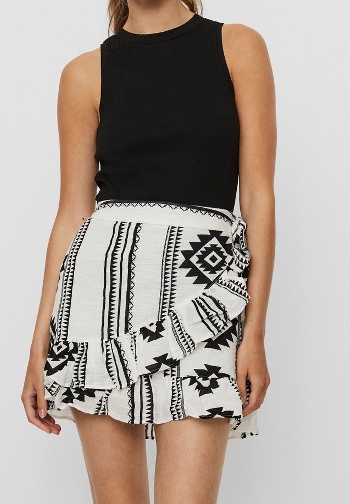 Haut sans manches noir à côtes associé à une jupe blanche courte ornée d'un motif tribal noir et d'un ourlet à volants.