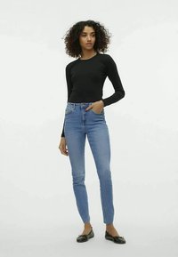 Blusa preta de manga longa combinada com jeans skinny azuis claros. Os jeans têm uma cintura média e um desbotado sutil, complementados por sapatos flats pretos.