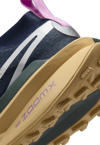 Zbliżenie na granatowe i beżowe buty biegowe Nike ZoomX z teksturowaną podeszwą, białym paskiem z logo oraz różową pętelką na pięcie.